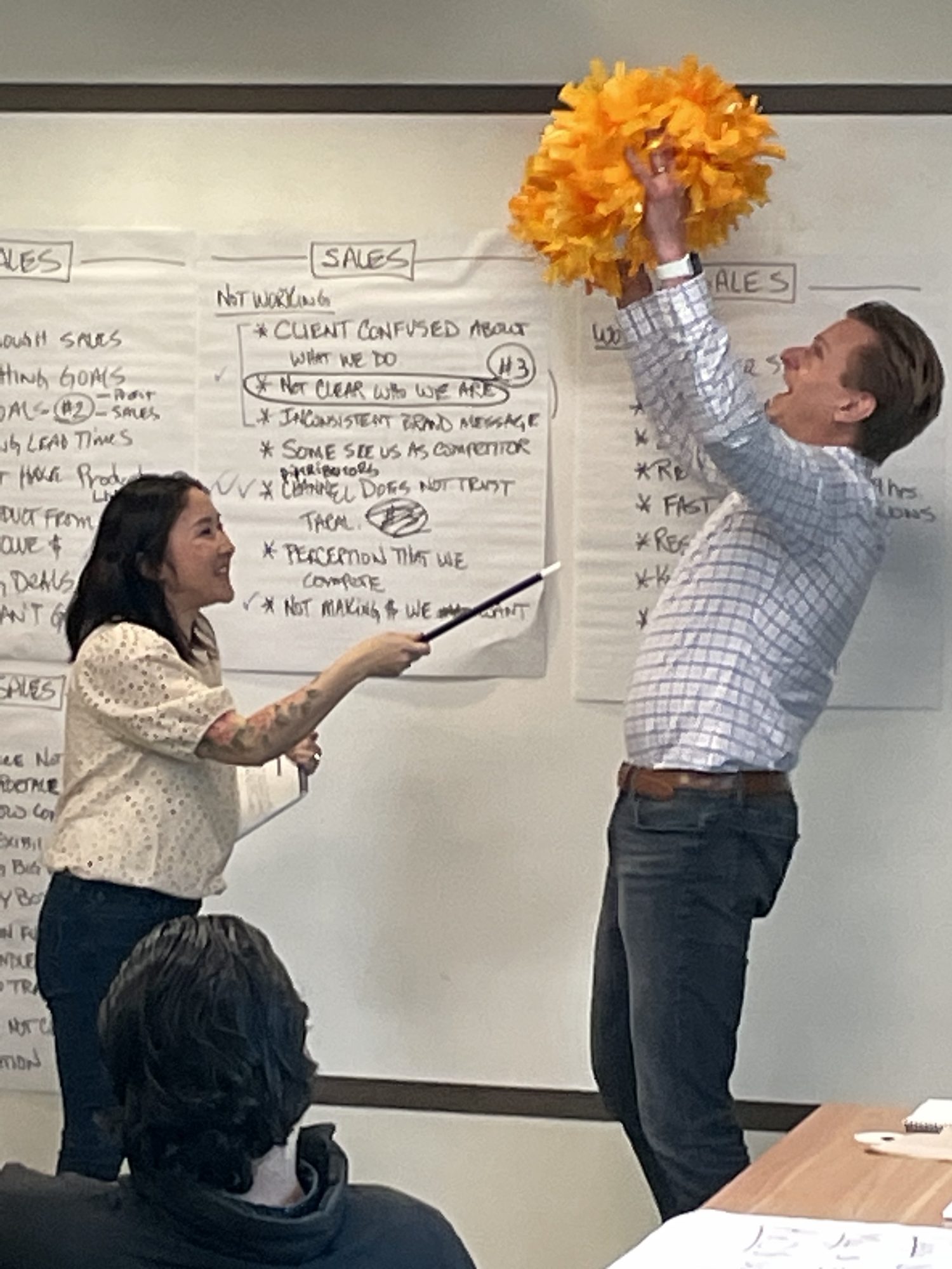 A workshop participant reaching for an orange pom-pom in front of a flip chart titled Sales, Not Working.