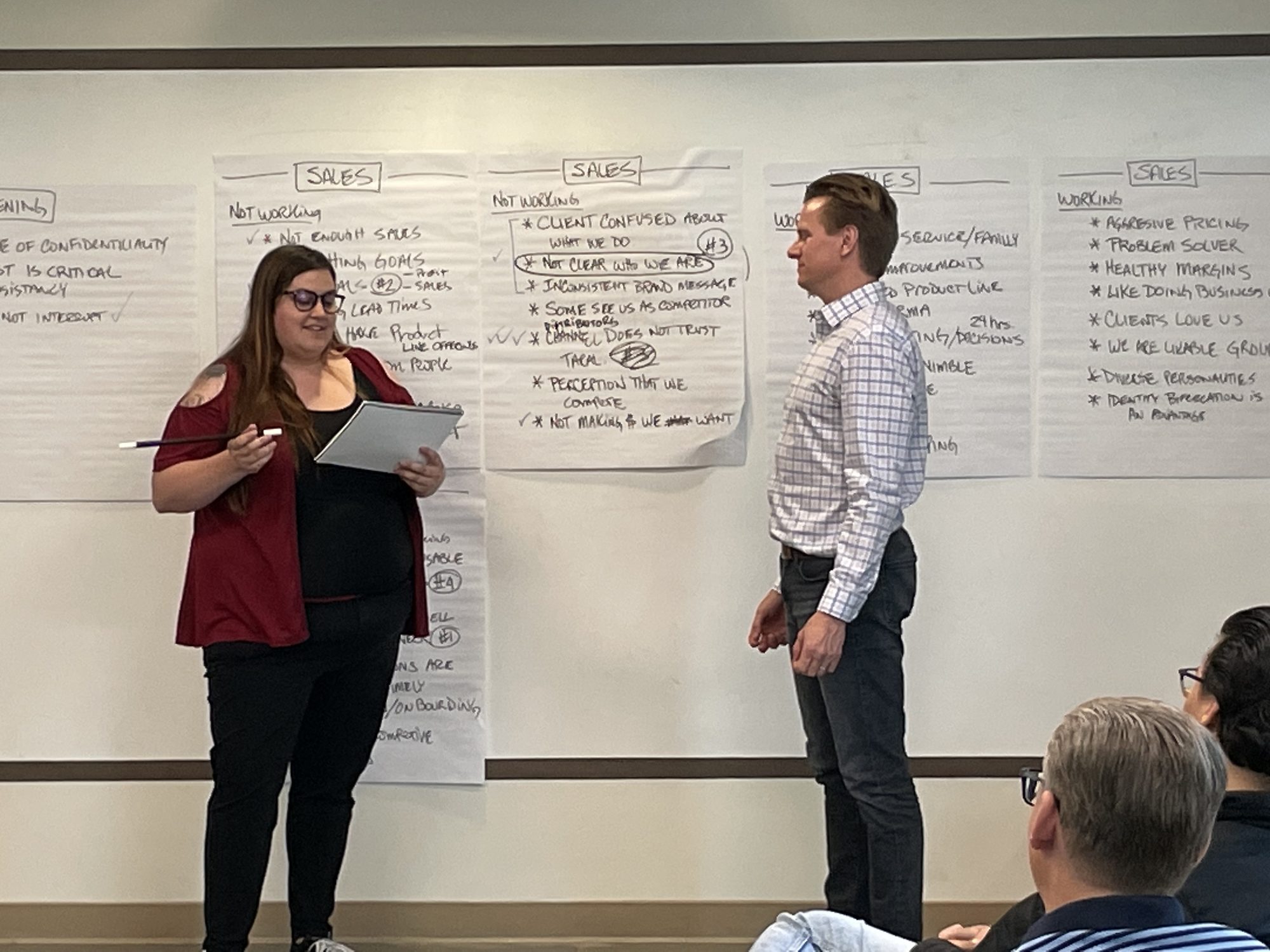 A woman reading from her notes beside a volunteer at the front of the room.