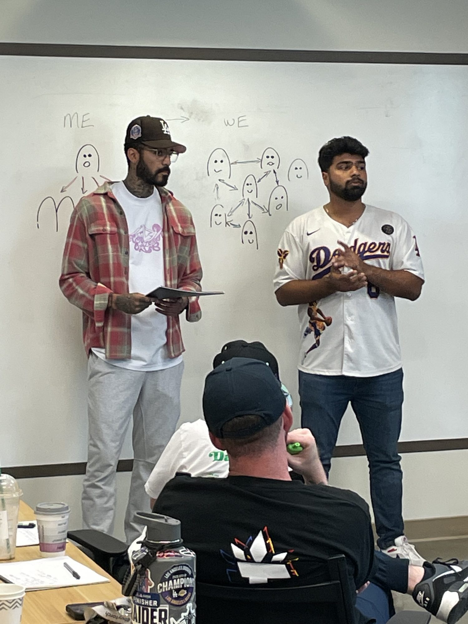 Two presenters standing in front of a Me to We whiteboard drawing.